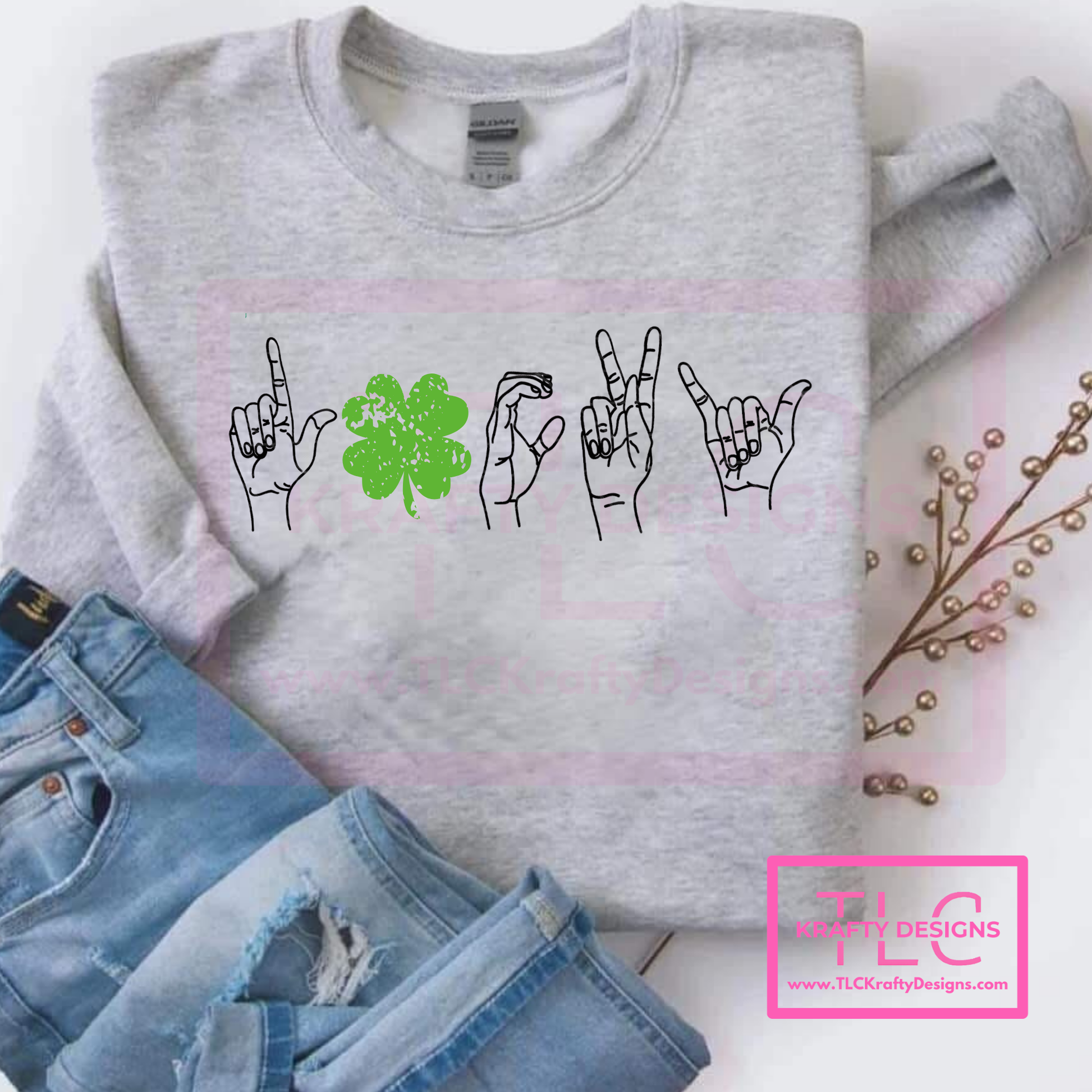 Gray sweatshirt with hand signs and a shamrock on a white background, next to denim jeans.