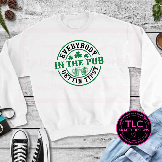 White sweatshirt with green Everybody Gettin' Tipsy Circular Design and shamrock design on a wooden surface, featuring the TLC Krafty Designs logo.