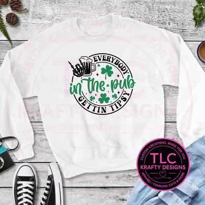 White sweatshirt with a printed everyone in the pub is getting tipsy design and 'TLC Krafty Designs' logo on a wooden surface.
