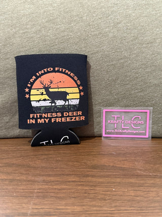 A black neoprene koozie with a humorous text design featuring a deer and the phrase 'I'm into fitness, deer in my freezer' displayed on a wooden surface with the brand name 'TLG' visible.