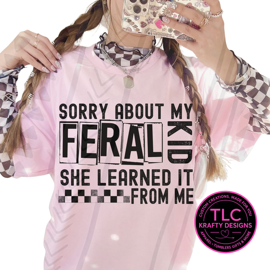 Person wearing a pink sweatshirt with sorry about my feral kid she gets it from me text and TLC Krafty Designs logo.