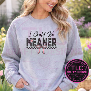 Person wearing a gray sweatshirt with 'I Could Be MEANER' text and a pink bow graphic, standing outdoors.