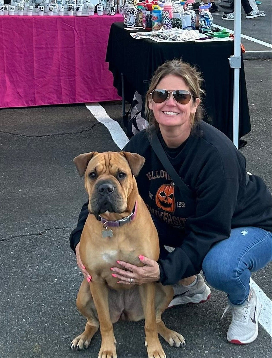 Woman with sunglasses and a dog at an outdoor market stall with various items on display.